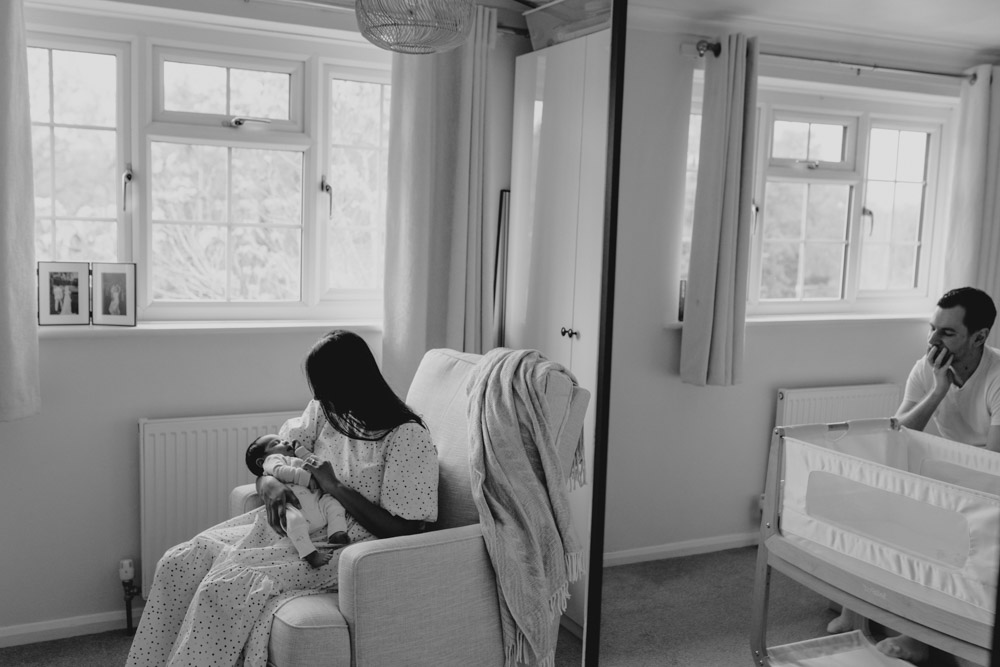 Mum is holding baby and sitting on the chair. Dad reflection is in the mirror. lovely capturing the moment photo session. Newborn photo shoot in Hampshire. Ewa Jones Photography