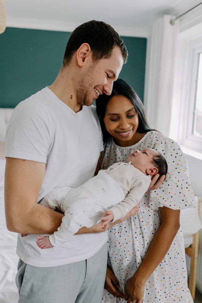 dad and mum are looking down and smiling to baby. Newborn session in your home. Natural photo shoot. Ewa Jones Photography