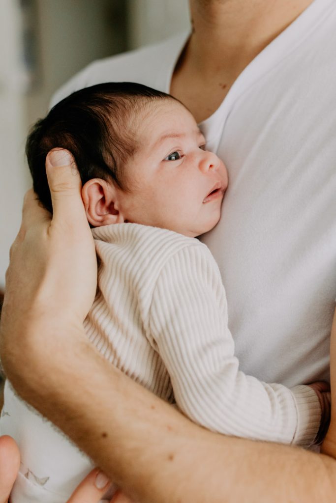 Close-up of a newborn baby in a neutral outfit being held by a parent during a natural in-home newborn photography session in Hampshire. Ewa Jones Photography