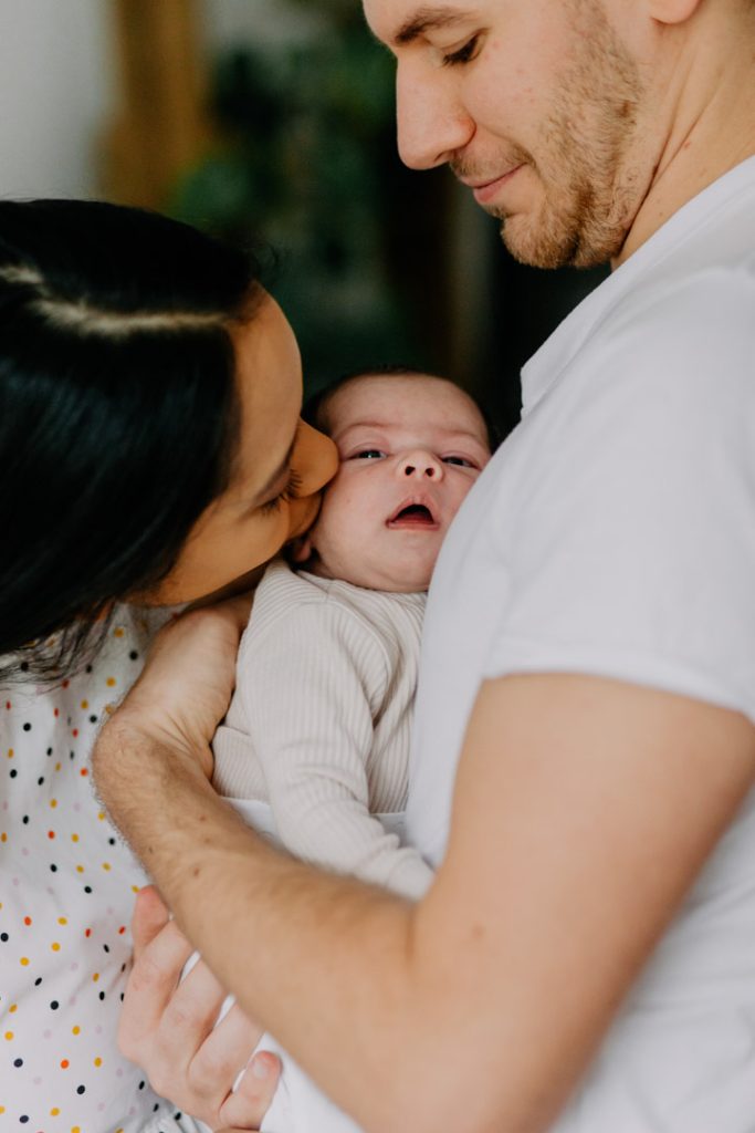 Mum and Dad gently cuddling their newborn baby together during a relaxed in-home newborn photography session in Hampshire. Ewa Jones Photography