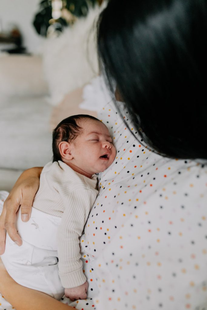 Mum is holding her baby in arms and looking at the baby. Baby is sleeping. In home natural newborn photo session. Ewa Jones Photography